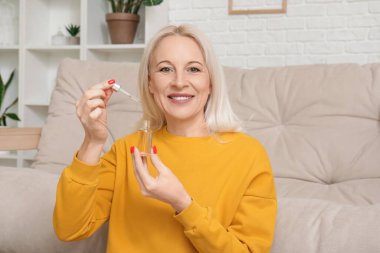 Mature woman with bottle of CBD oil at home clipart