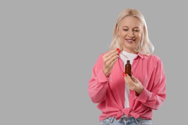 Gri arka planda bir şişe CBD yağı olan olgun bir kadın.