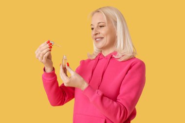 Sarı arka planda bir şişe CBD yağı olan olgun bir kadın.