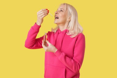 Sarı arka planda CBD yağı alan olgun bir kadın.