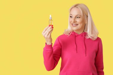 Mature woman with bottle of CBD oil on yellow background clipart