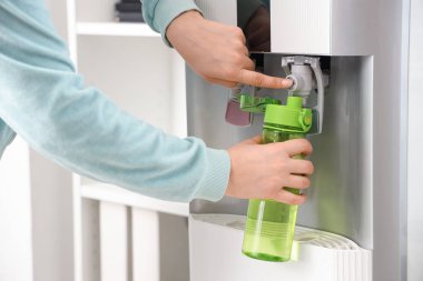 Yeşil şişeyi soğutucudan filtrelenmiş suyla dolduran kadın elleri