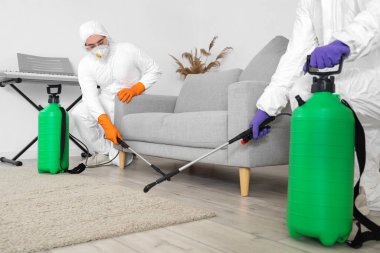 Tehlikeli madde giysileri içinde erkek işçiler zemin katını dezenfekte ediyor.