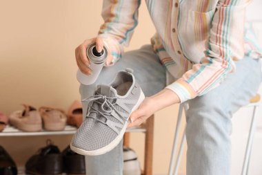 Evdeki spor ayakkabısına su püskürtücü sprey sıkan kadın, yakın plan.