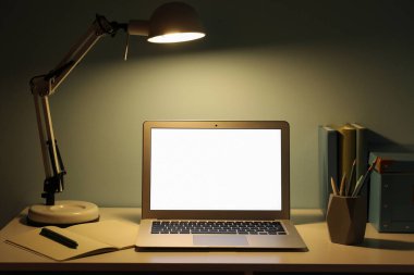 Modern dizüstü bilgisayarı ve yeşil duvarın yanında parlayan lambası olan işyeri