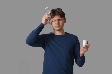 Gri arka planda baş ağrısı çeken bir şişe su ve haplı genç adam.