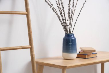 Oturma odasındaki masada söğüt dalları ve kitapları olan vazo.