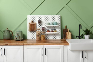 Mutfaktaki yeşil duvarın yanında tahta, yemek takımı ve ev bitkisi.