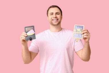 Cüzdanları ve kredi kartlarını pembe arka planda tutan genç adam.