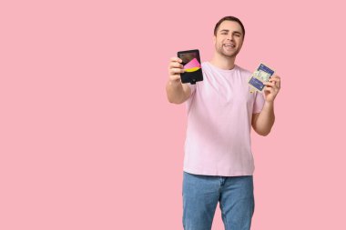 Cüzdanları ve kredi kartlarını pembe arka planda tutan genç adam.