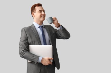 Gri arka planda bir fincan taze kahve ve dizüstü bilgisayar tutan genç adam.