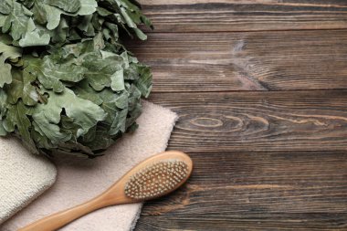 Meşe saunası süpürgesi, masaj fırçası, sünger ve havlu ahşap arka planda.