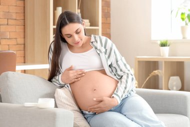 Genç hamile kadın evdeki kanepeye krem sürüyor.