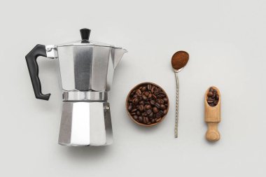 Gayzer kahve makinesi, bir kase fasulye ve beyaz arka planda bir kaşık öğütülmüş kahve. Üst görünüm