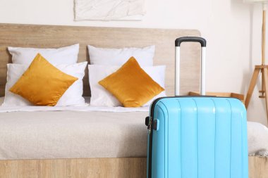 Otel odasının içinde, yatağın yanında bavul var.
