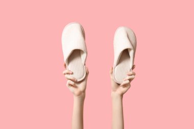 Pembe arka planda açık renk terlikler tutan kadın eller.