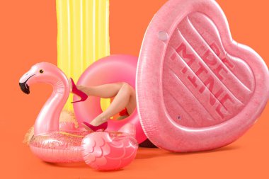 Topuklu giyen genç bir kadın turuncu arka planda şişme yüzüklerin üzerinde yatıyor. Seyahat kavramı