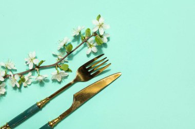 Turkuaz arka planda çiçek açan dallı altın çatal bıçak seti
