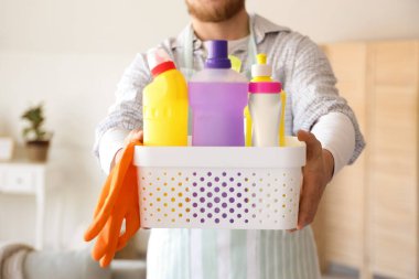 Young man with cleaning supplies at home, closeup