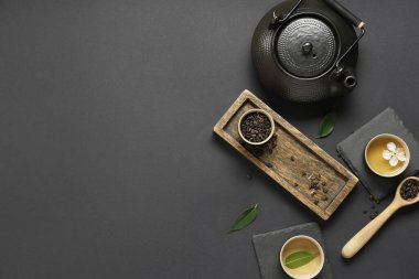 Fincanlı çaydanlık, bir kaşık kuru çay ve siyah arka planda yapraklar.