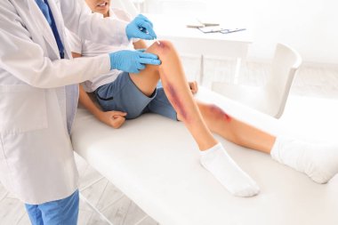 Küçük çocuğun yaralı bacağını klinikte tedavi eden kadın doktor, yakın plan.