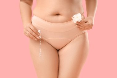 Dönem külotlu genç kadın pembe arka planda çiçekli tampon tutuyor.