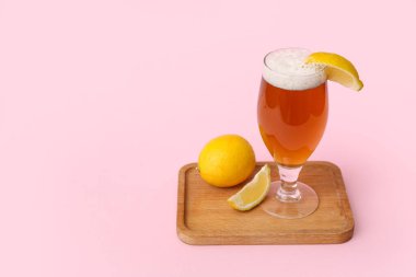 Pembe arka planda limonlu bir bardak taze bira.