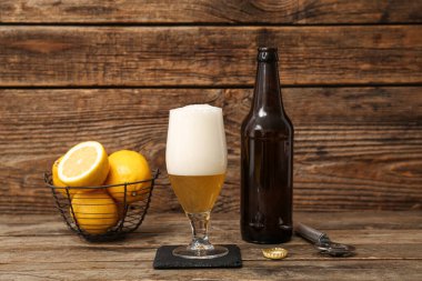 Ahşap arka planda limonlu bir şişe ve bir bardak taze bira.