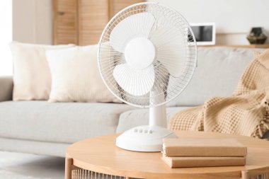Oturma odasının içinde, kahve masasında modern elektrikli vantilatör var.