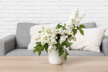 Oturma odasındaki kanepenin yanındaki sehpanın üzerinde leylak dalları olan vazo.