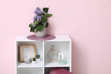 Odadaki pembe duvarın yanındaki raflarda leylak dalları olan vazo.