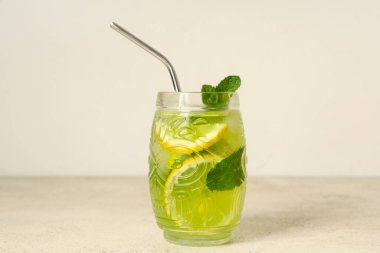 Limon dilimli bir bardak lezzetli limonata, beyaz arka planda nane ve saman.