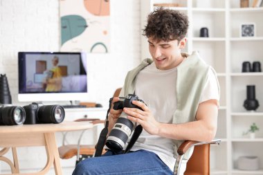 Farklı kameraları olan profesyonel mutlu erkek fotoğrafçı stüdyoda oturuyor.