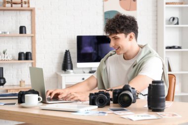 Modern kameraları ve laptopu olan profesyonel mutlu erkek fotoğrafçı stüdyoda çalışıyor.