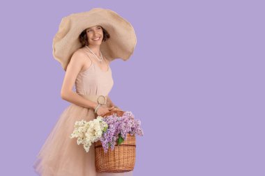 Beautiful young woman holding wicker basket with bouquet of blooming lilac flowers on color background