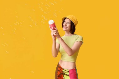 Sarı arka planda sabun köpüğü tabancası olan mutlu genç kız.