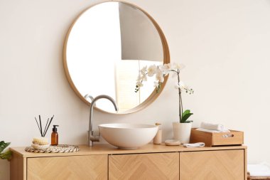 Lavabosu, aynası ve banyo aksesuarları olan ahşap bir dolap.