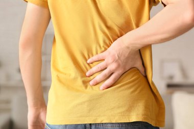 Handsome young man suffering from back pain at home, closeup