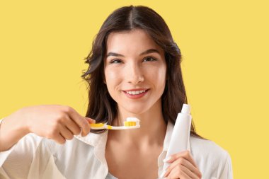 Sarı arka planda diş fırçası ve yapıştırmasıyla gülümseyen genç kadın, yakın plan.
