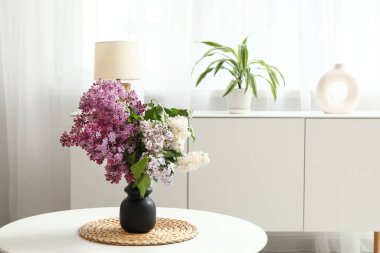 Işık odasındaki çekmecelerin yanındaki masanın üzerinde leylak dalları olan vazo.