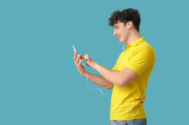 Kulaklıklı, tablet bilgisayarlı yakışıklı genç adam mavi arka planda müzik dinliyor.