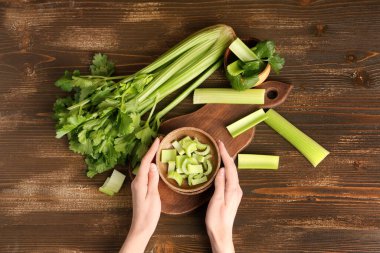 Ahşap zemin üzerinde bir kase taze yeşil kereviz ile kadın elleri.