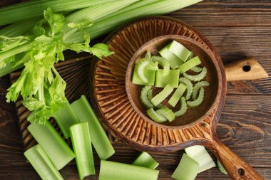 Tahta zemin üzerinde taze yeşil kereviz olan kase ve tahtalar.