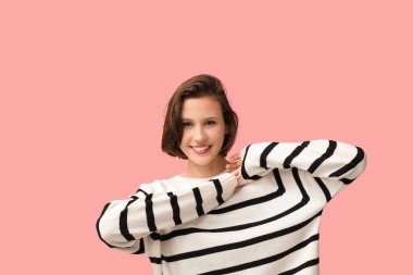 Pembe arka planda şık çizgili süveter giyen güzel genç bir kadın.