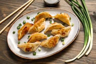 Kızarmış Japon gyoza tabağı ve ahşap arka planda yeşil soğan.