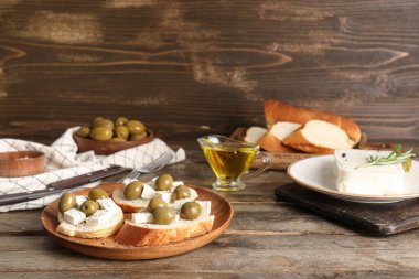 Lezzetli peynirli ekmek dilimleri ve ahşap zemin üzerinde zeytinler.