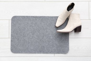 Koridordaki beyaz zeminde gri kapı paspası ve ayakkabılar