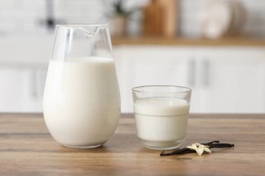 Bardak ve sürahi taze vanilya sütü. Mutfaktaki ahşap masada çiçek ve sopalarla.