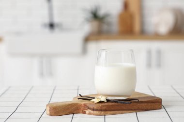 Bir bardak taze vanilya sütü, çubuklu ve çiçekli mutfak fayanslarının üzerinde.