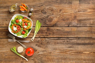 Bir kase taze sebze salatası, dolmalık biber ve ahşap arka planda beyaz peynir.